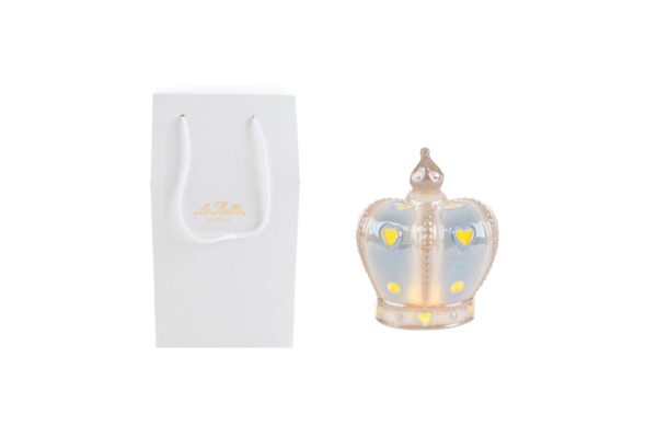 Corona in porcellana LED celeste 9x8x4,5 cm accesa accanto a shopper bianco con dettagli decorativi dorati.