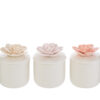 Tre candele in scatole di porcellana bianca con coperchi decorati da fiori tridimensionali nei colori rosa, crema e bianco.