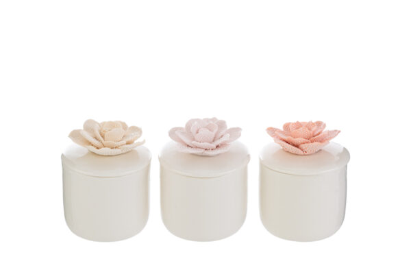 Tre candele in scatole di porcellana bianca con coperchi decorati da fiori tridimensionali nei colori rosa, crema e bianco.