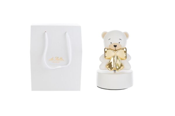 Carillon a forma di orsetto in porcellana bianca con fiocco dorato, 9xH14 cm, accanto a shopper bianco abbinato.