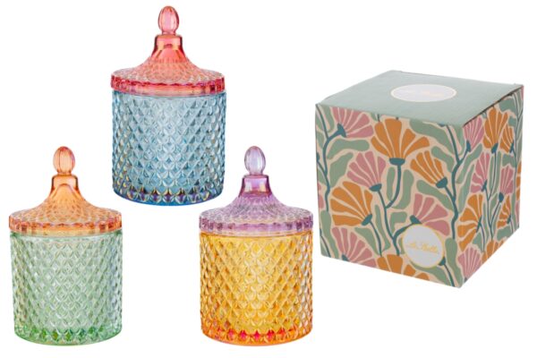 Tre scatole in vetro colorato con coperchio, disponibili in tre colori assortiti, accanto a una confezione decorata.