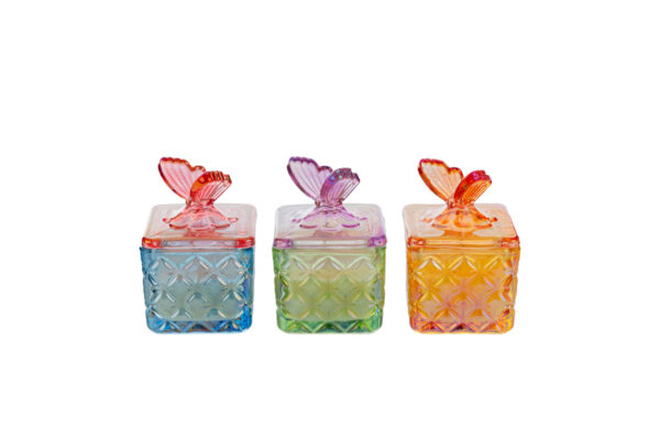 Tre candele in scatole di vetro colorato con decorazioni a farfalla, disponibili in tre colori assortiti: blu, verde e arancione.